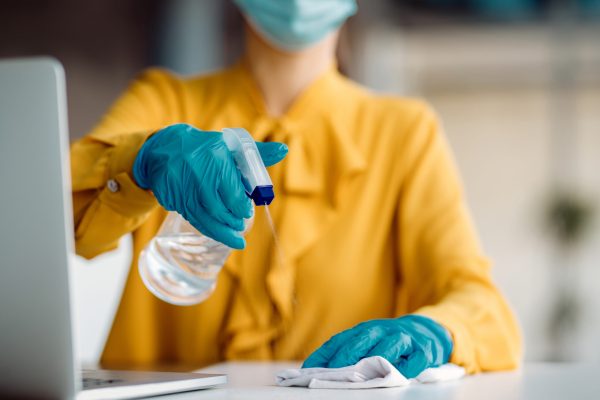 Close-up of businesswoman disinfecting her desk in the office due to coronavirus pandemic.