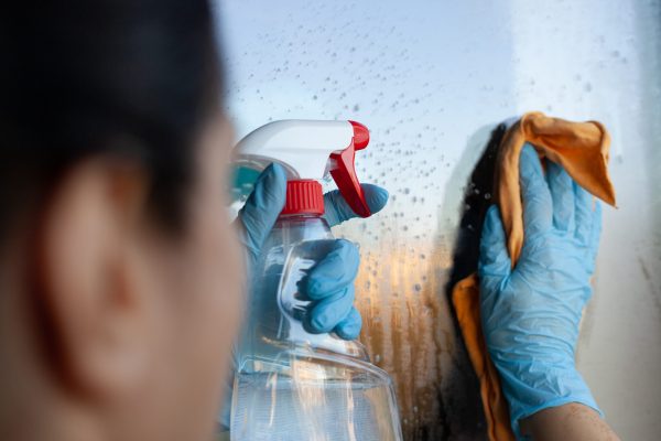 A female wearing blue gloves cleaning window with yellow cloth