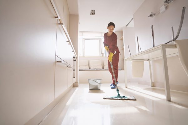 Full-length portrait of concentrated janitor cleaning floor with long-handled microfiber wet mop